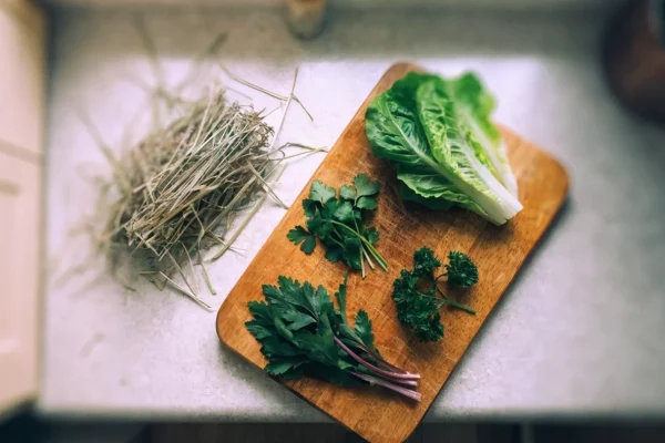 Fresh leafy greens and timothy hay arranged on a cutting board — staples of a healthy rabbit diet